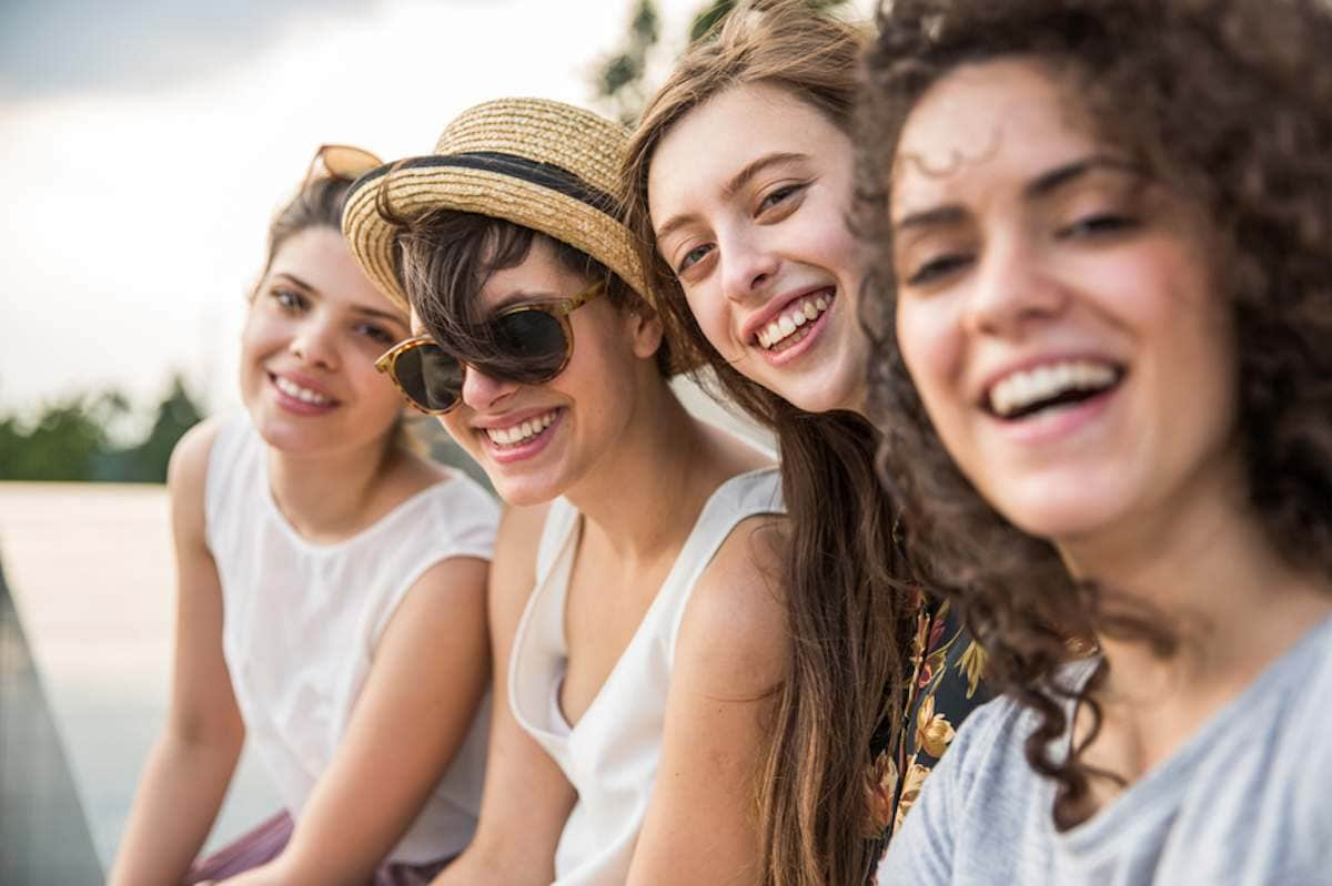 Four young women are sitting outside and taking a selfie together