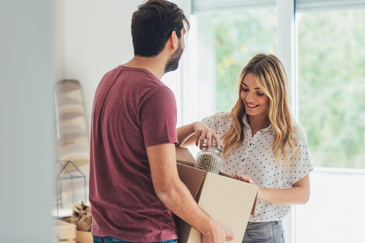 Young woman unpacking moving box held by her boyfriend