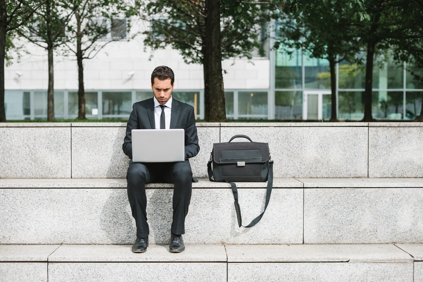 Business man working on his laptop outside of an office building.