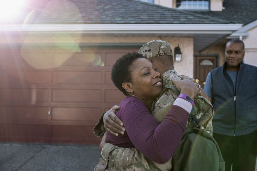 Affectionate soldier son and mother hugging in driveway