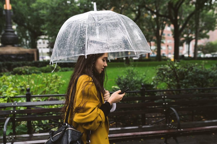 Woman standing in the rain with an umbrella and reading on her smart phone.