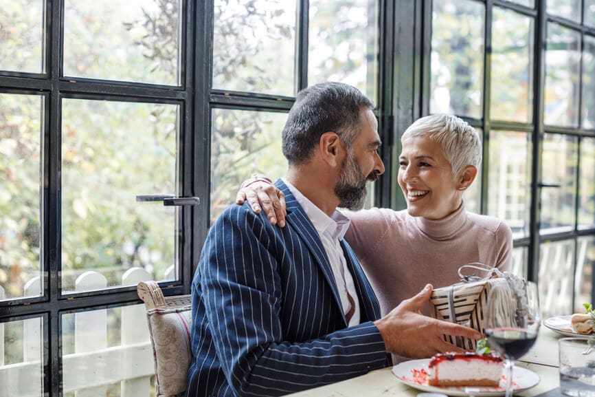 Husband giving wife an anniversary present at a restaurant.