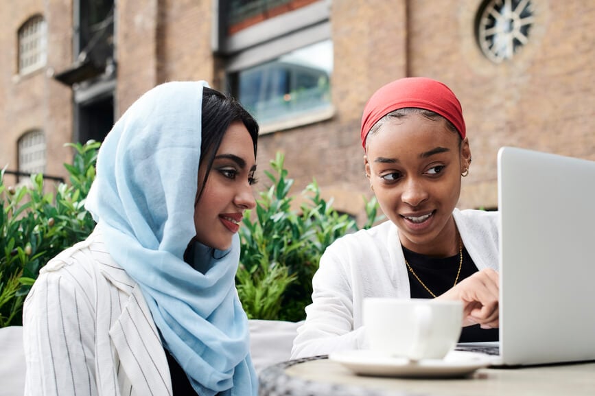 Muslim girl friends using sitting in a cafe having tea and reading from a laptop.