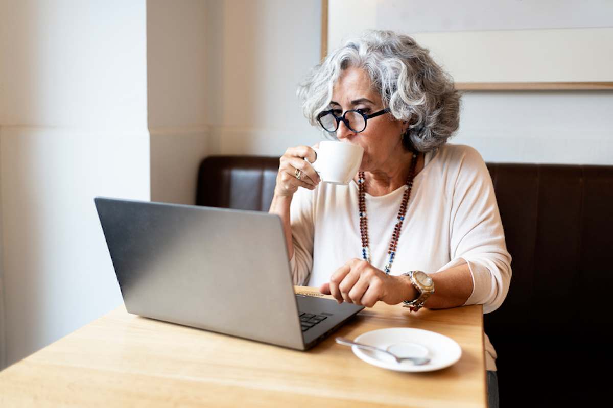 Mature woman sips coffee while using a laptop in a cafe