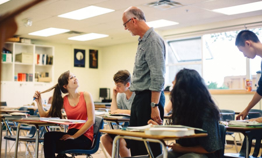 Male teacher helping high school students in a classroom.