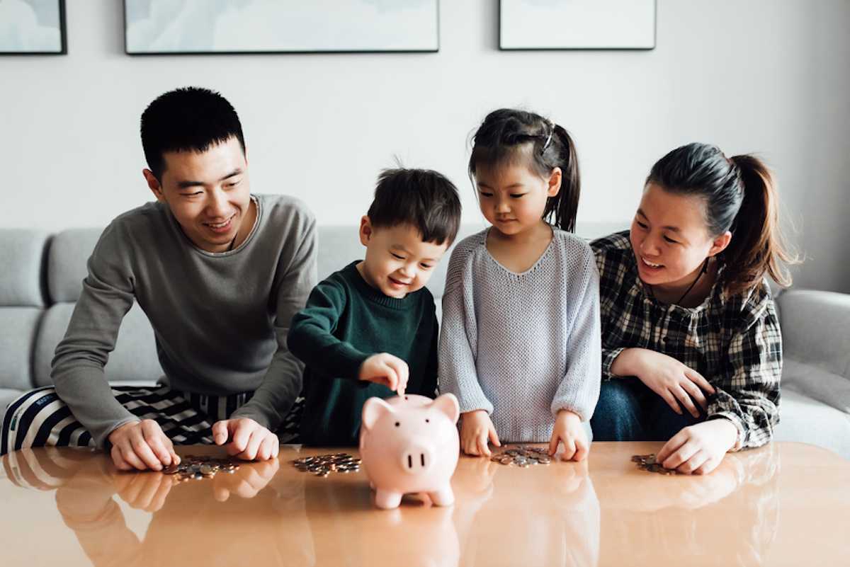 Parents with two young children putting money into a piggy bank