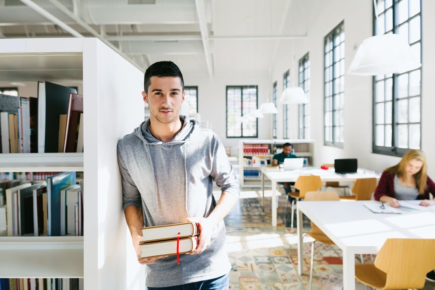 Young University Man Holding Books In A Library.