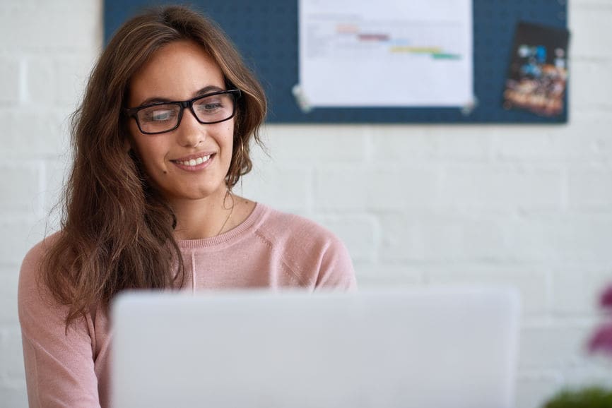 Woman smiling while working on laptop from home office desk