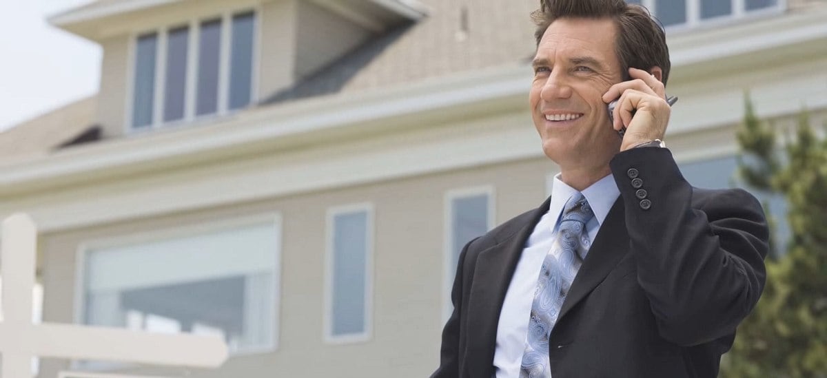 smiling man using a mobile phone outside a home