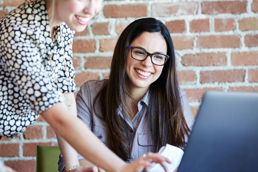 Close-up of Millennial Hispanic woman working at computer with a female friend