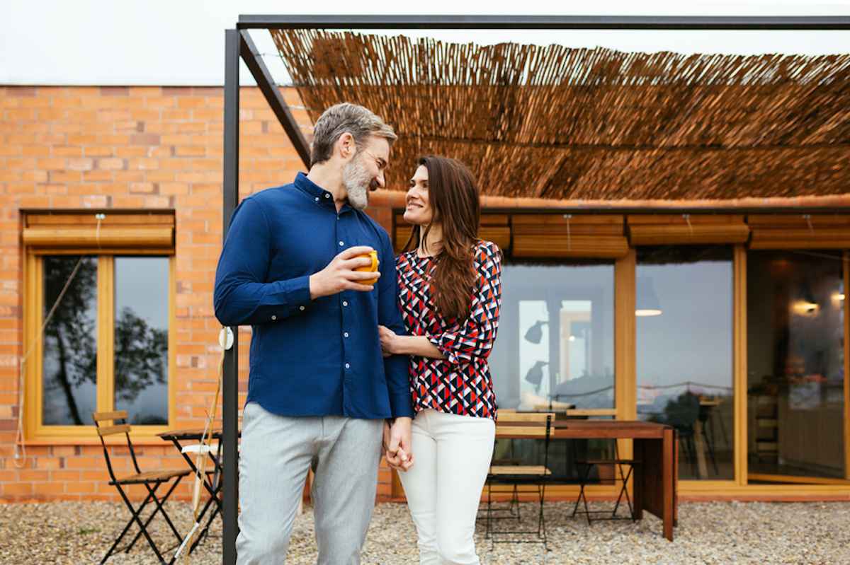 A couple standing in their backyard smile at each other.