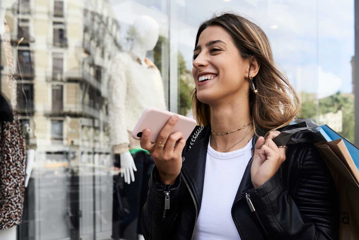 Stylish woman carrying shopping bags walks down the street and talks on mobile phone