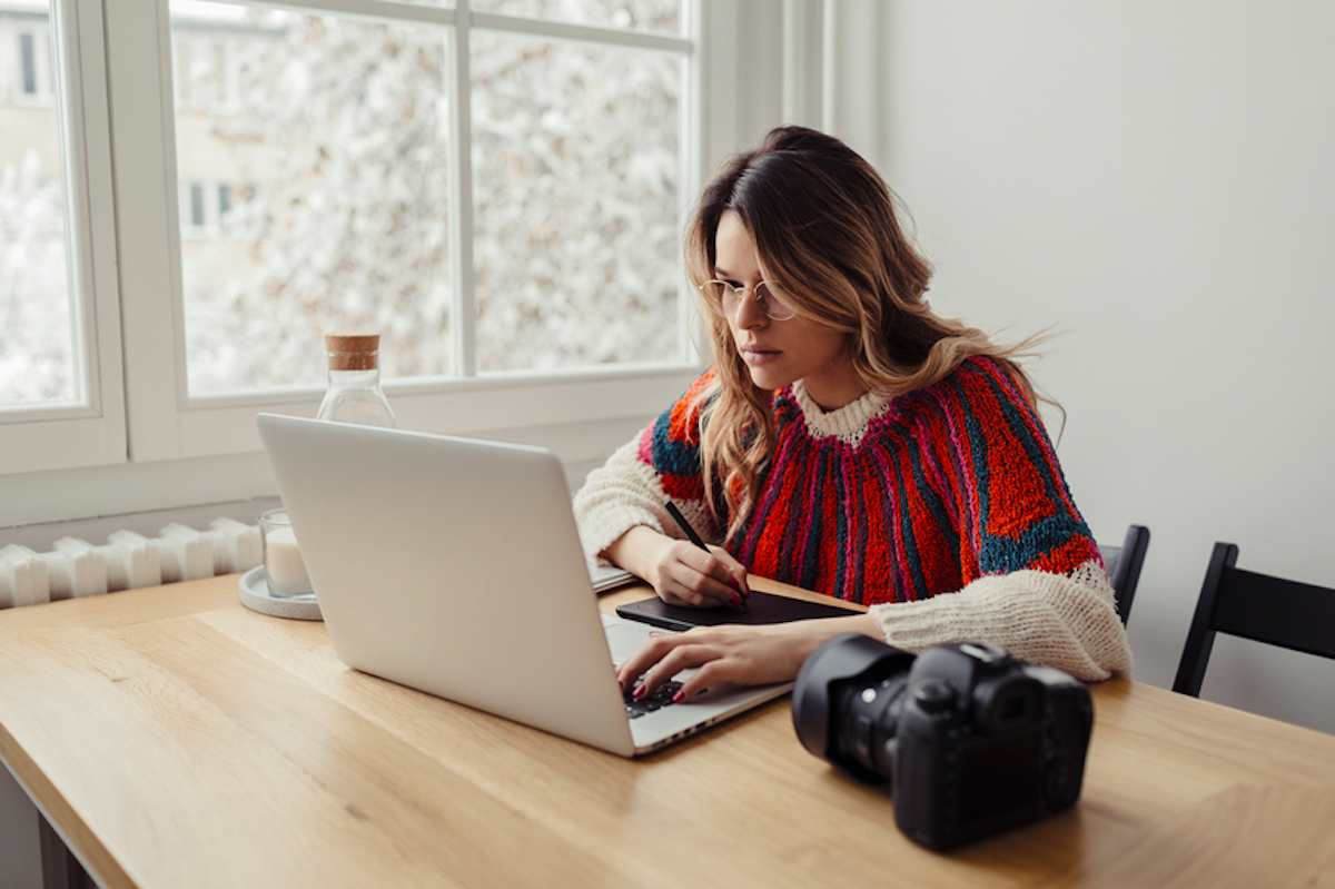 Young female photographer working on computer on a table by a window