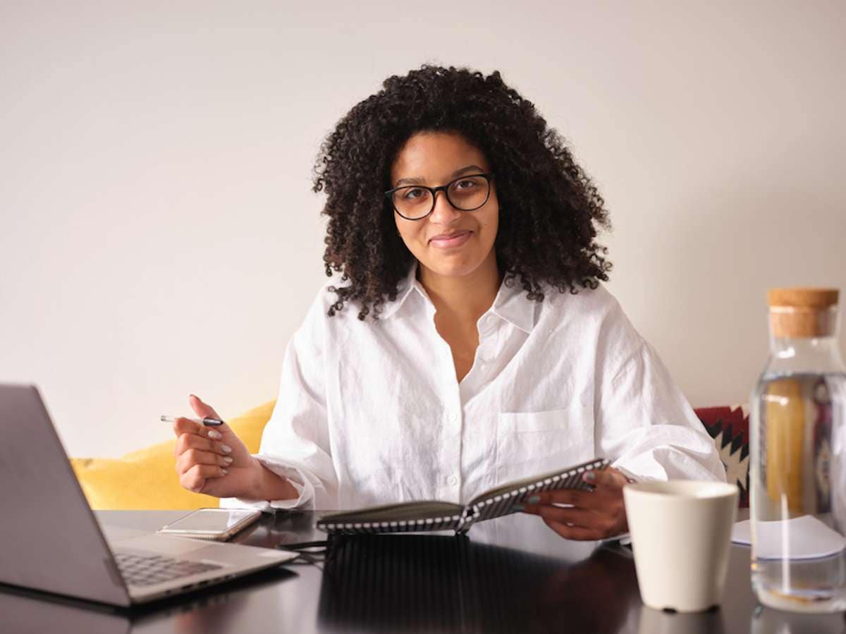 Businesswoman wearing eyeglasses holds a pen and an open planner while sitting at a desk
