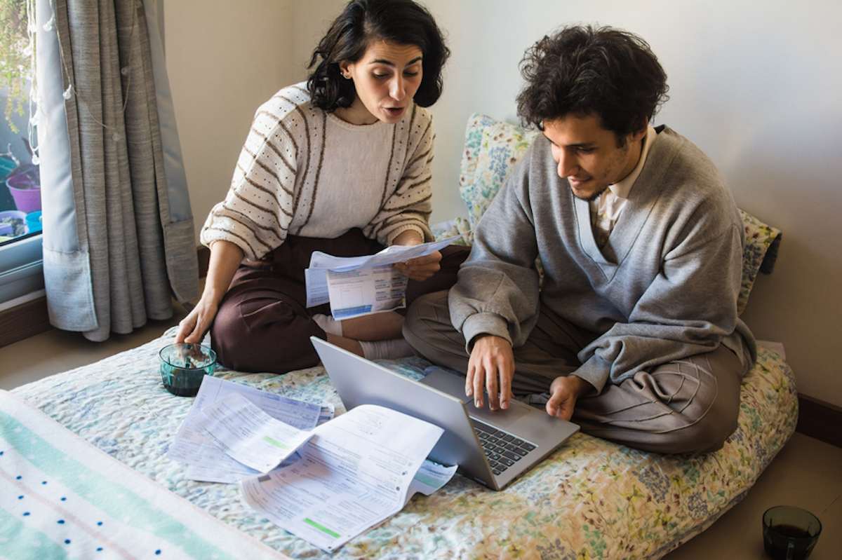 Couple sitting in a mattress on the floor works on their personal finances