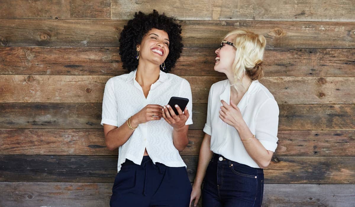 Businesswomen at office looking at mobile phone laughing