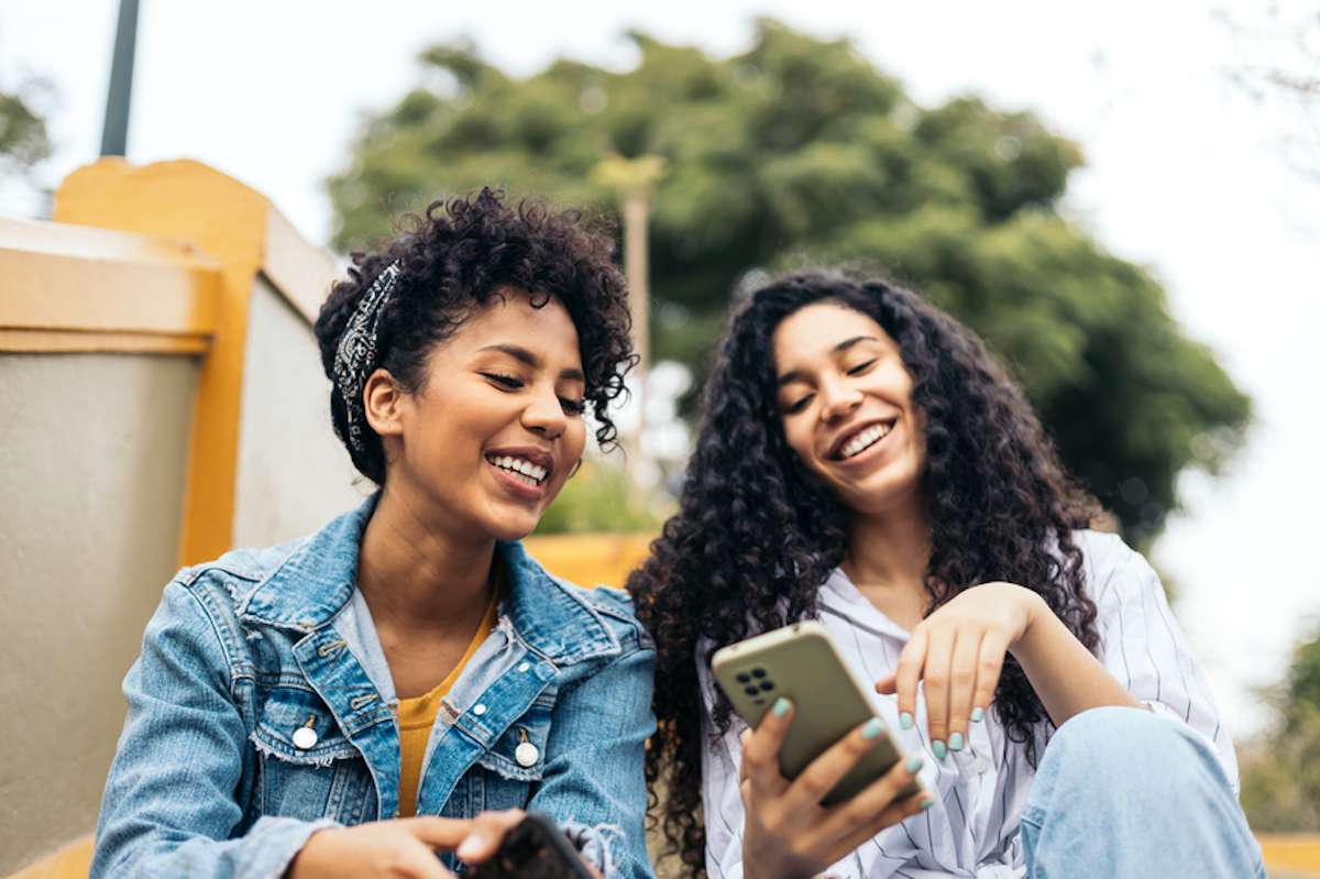 Two young women sitting on stairs outside use a smartphone together