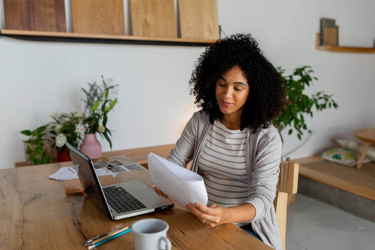 A Black woman seated at a desk looks over paperwork.