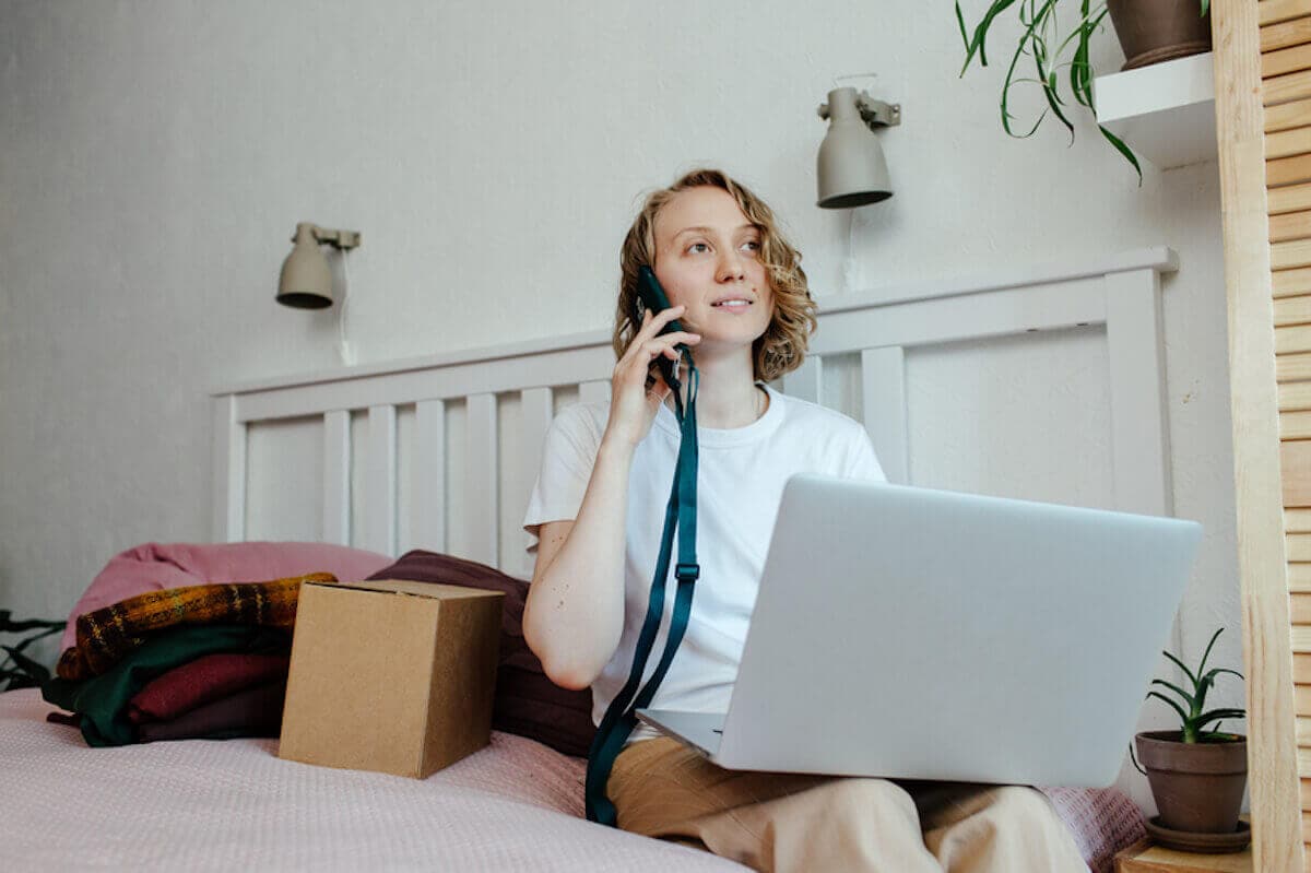 Young woman with laptop computer in her lap uses cell phone