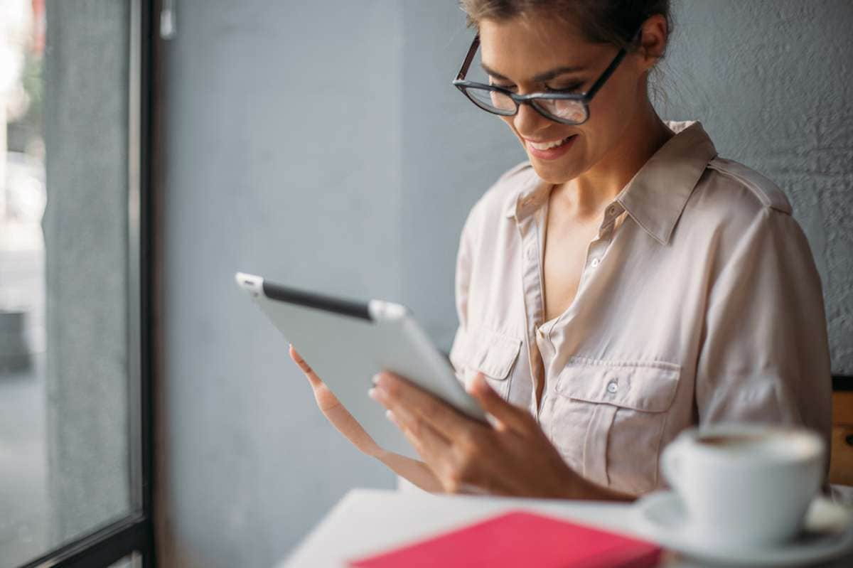 Woman wearing eyeglasses uses a tablet in a coffee shop