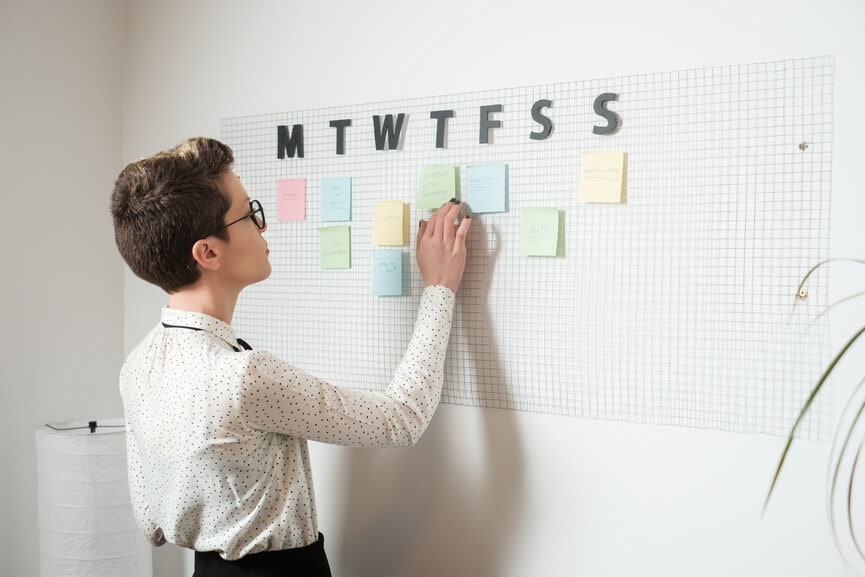 Young stylish woman updating her weekly schedule on the office wall.