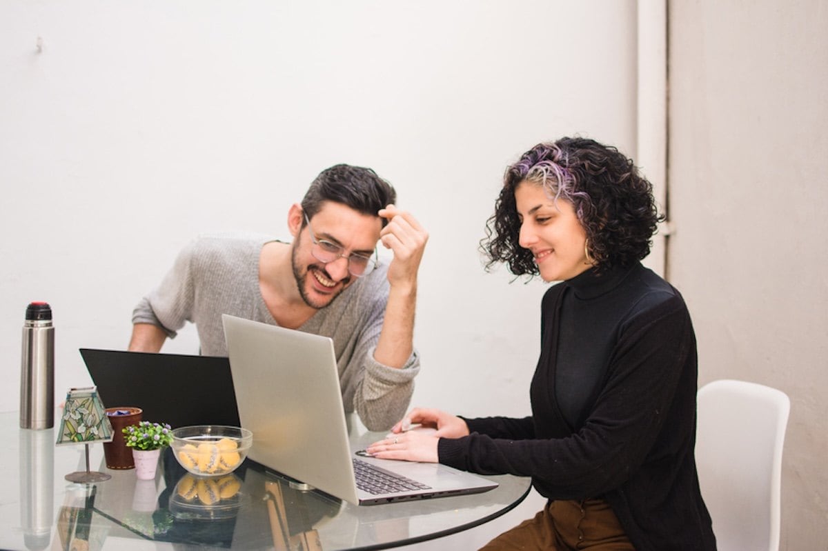 A person and person sitting at a table with laptops.