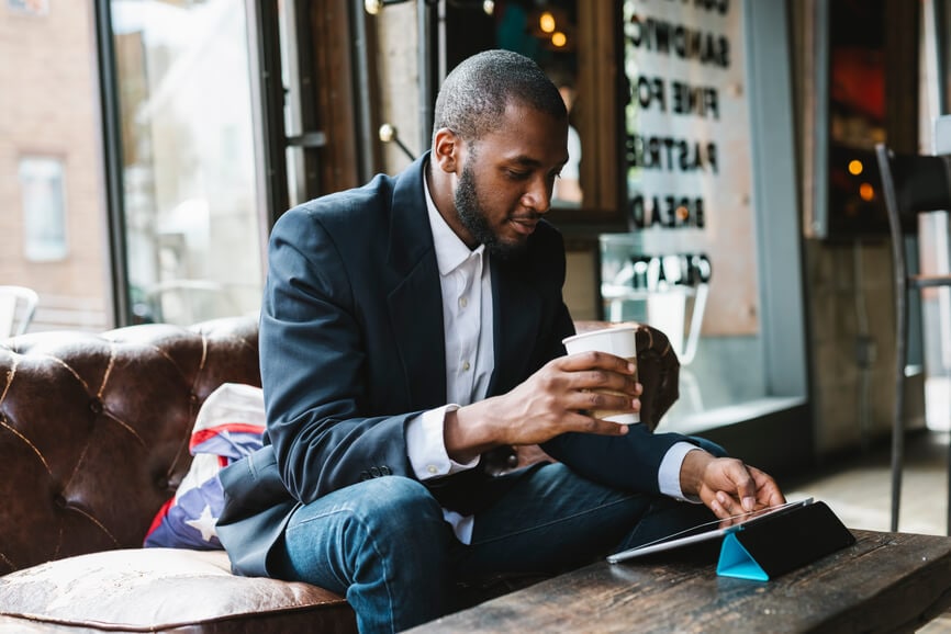 A young man in a coffee shop checking his investments on his tablet.