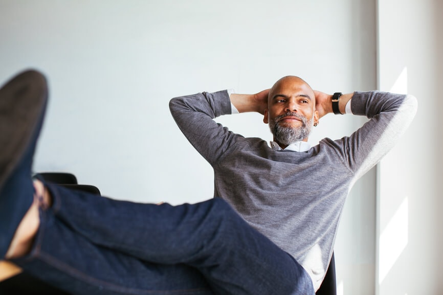 Man smiling with his feet on his desk and leaning back comfortably in his chair.