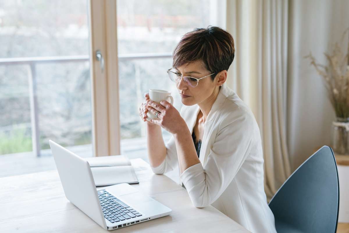 Businesswoman holding a mug of coffee works on laptop from home
