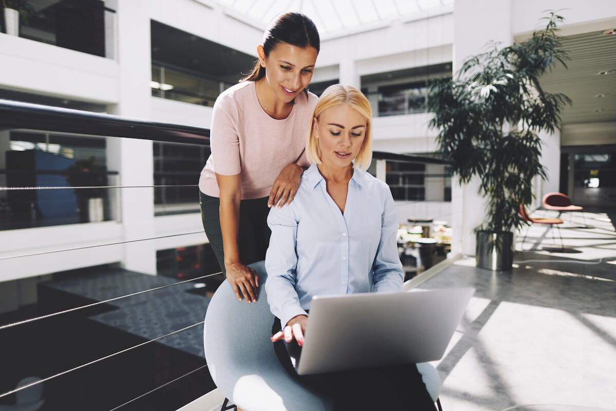 Two professional women collaborate on a laptop. 