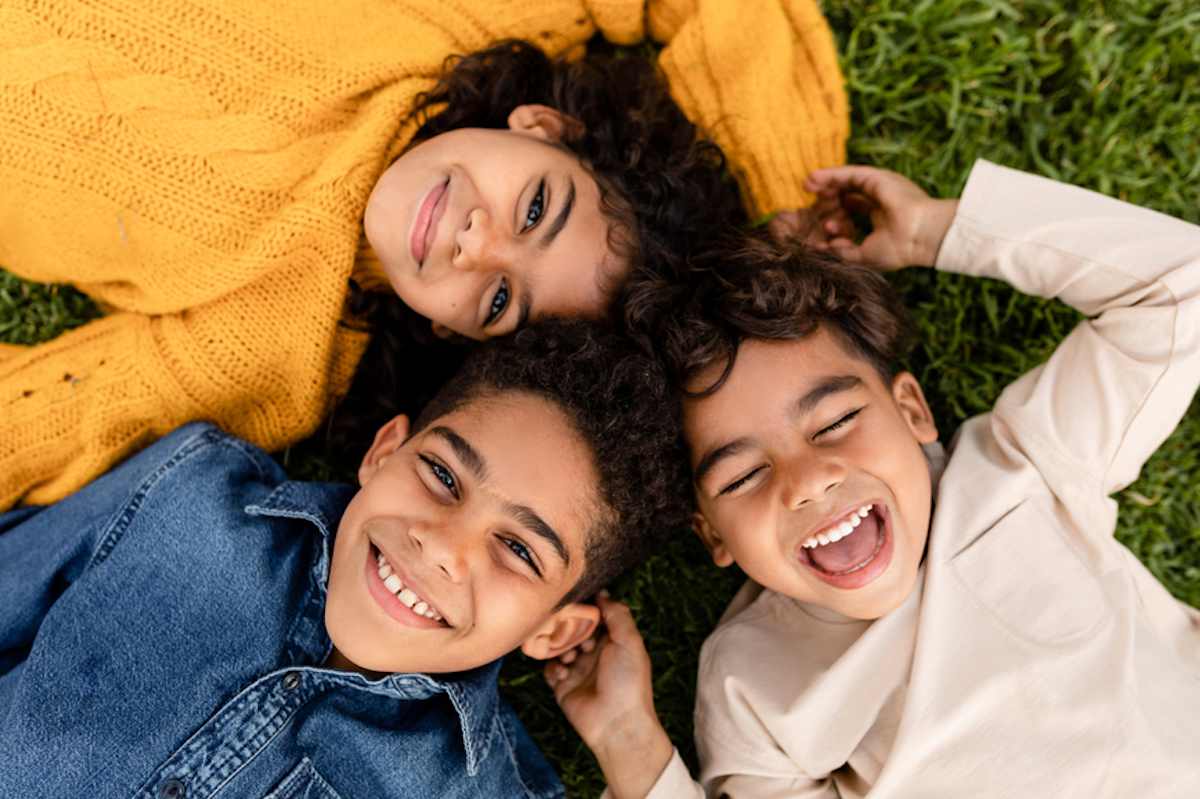 Tres niños sonrientes yacían juntos en un césped.