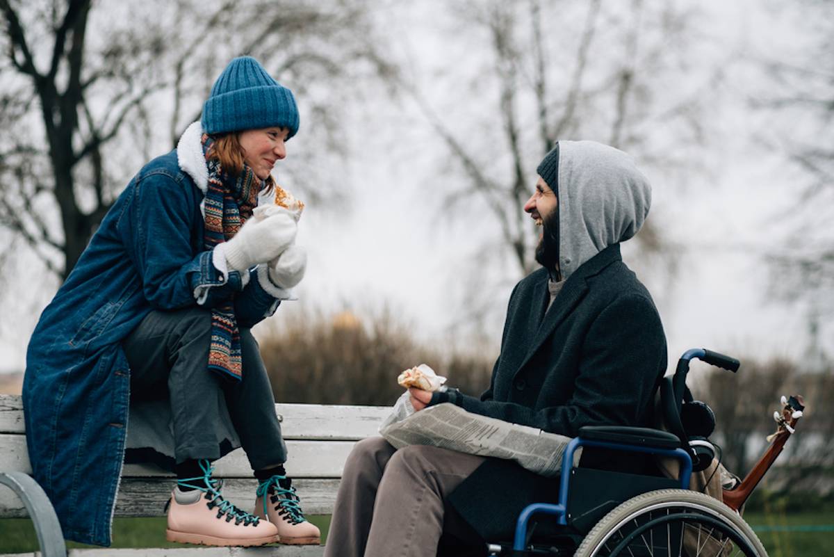 person in wheelchair eating with friend in a park