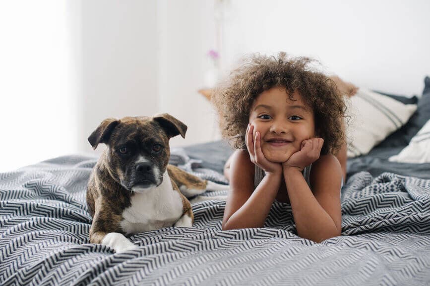 Child smiling in bed with her puppy.