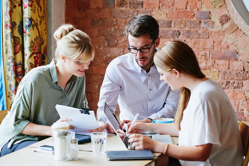 Three office workers reviewing documents together at table