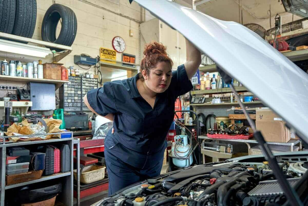 A mechanic looks under the hood of a car. 