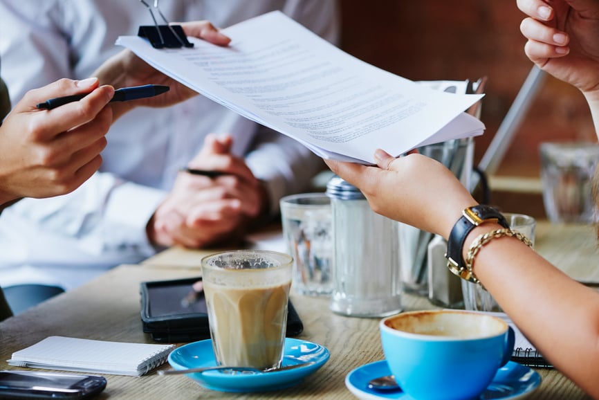 papers handed across table at coffee shop
