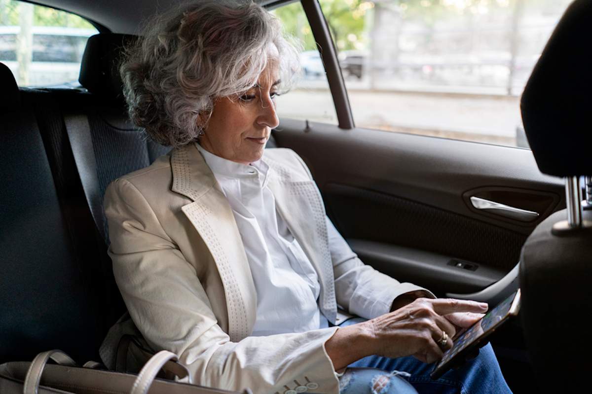 Mature woman uses her cell phone in the backseat of a car