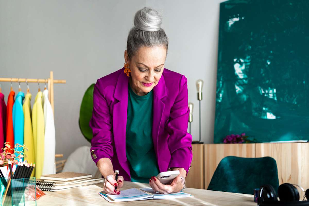 Stylish mature woman checks her smartphone and writes in a notebook