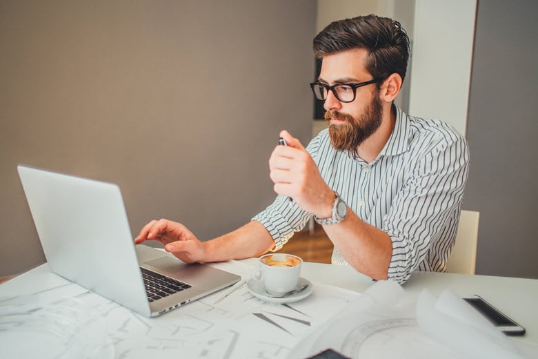 Man working on laptop holding pen