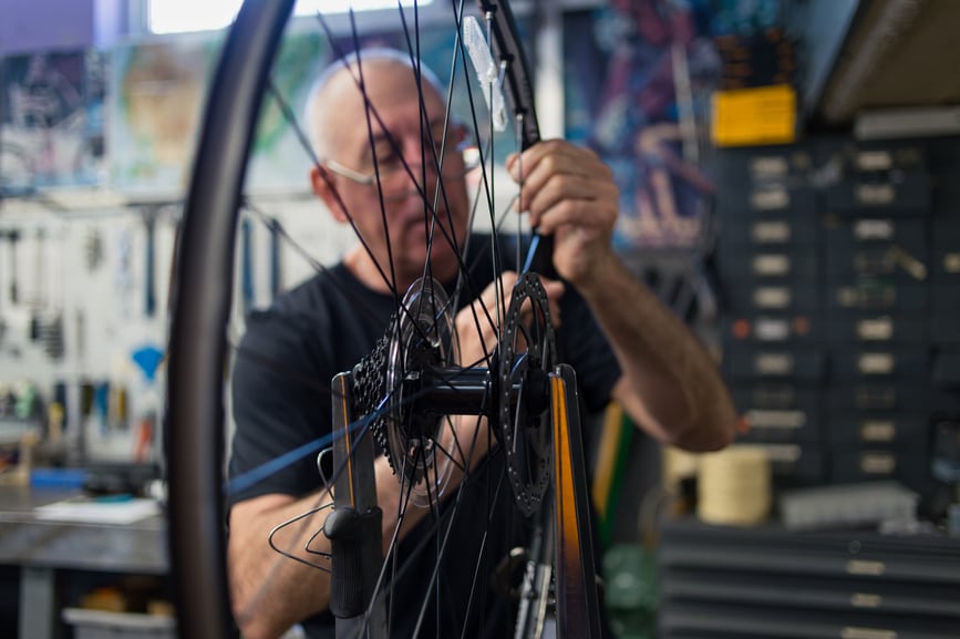 An older man with glasses works on repairing a bicycle wheel.