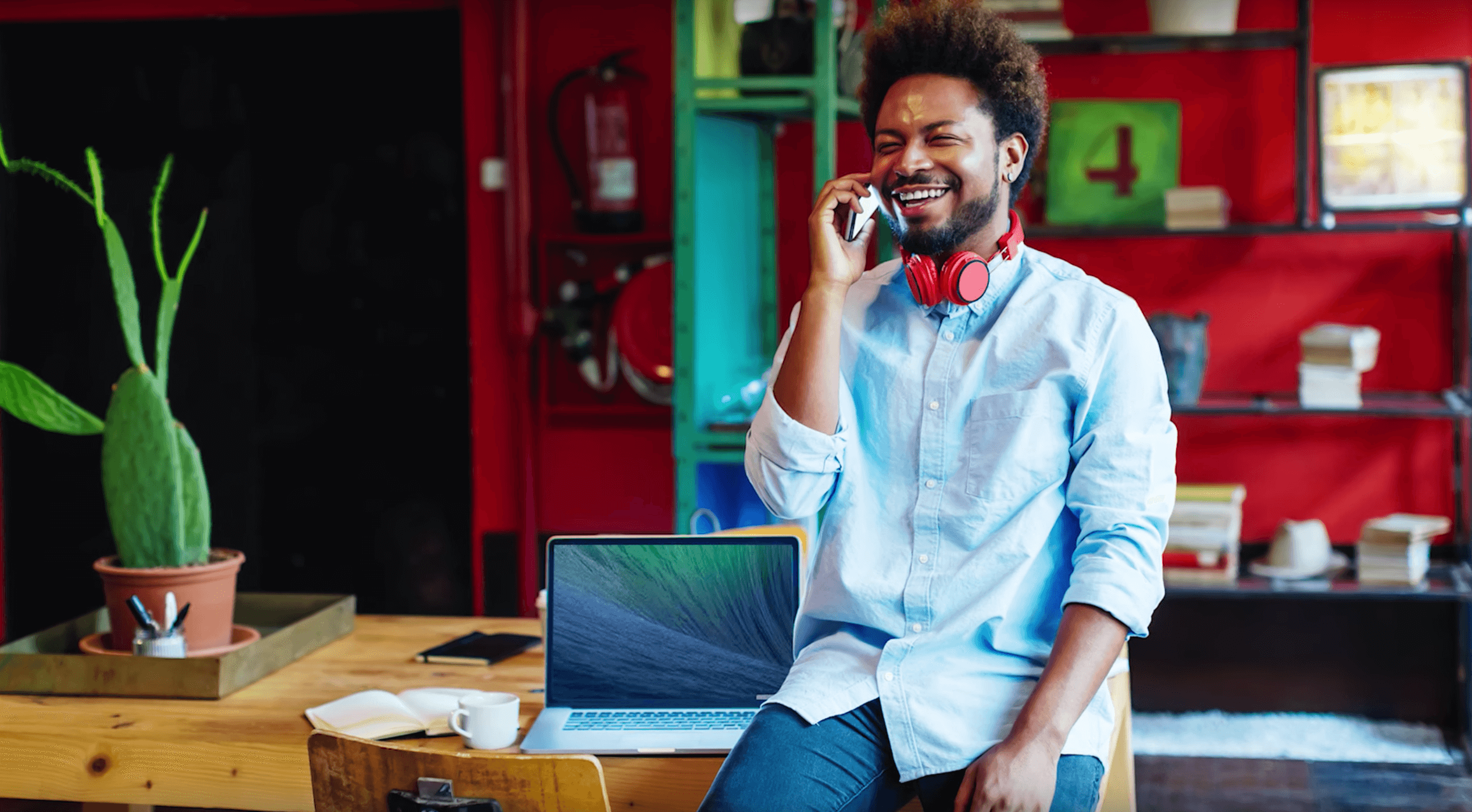 Smiling man sitting on a desk and talking on his cell phone