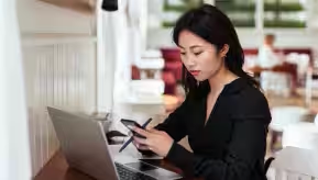 Una mujer en su escritorio con un tel. y una laptop.