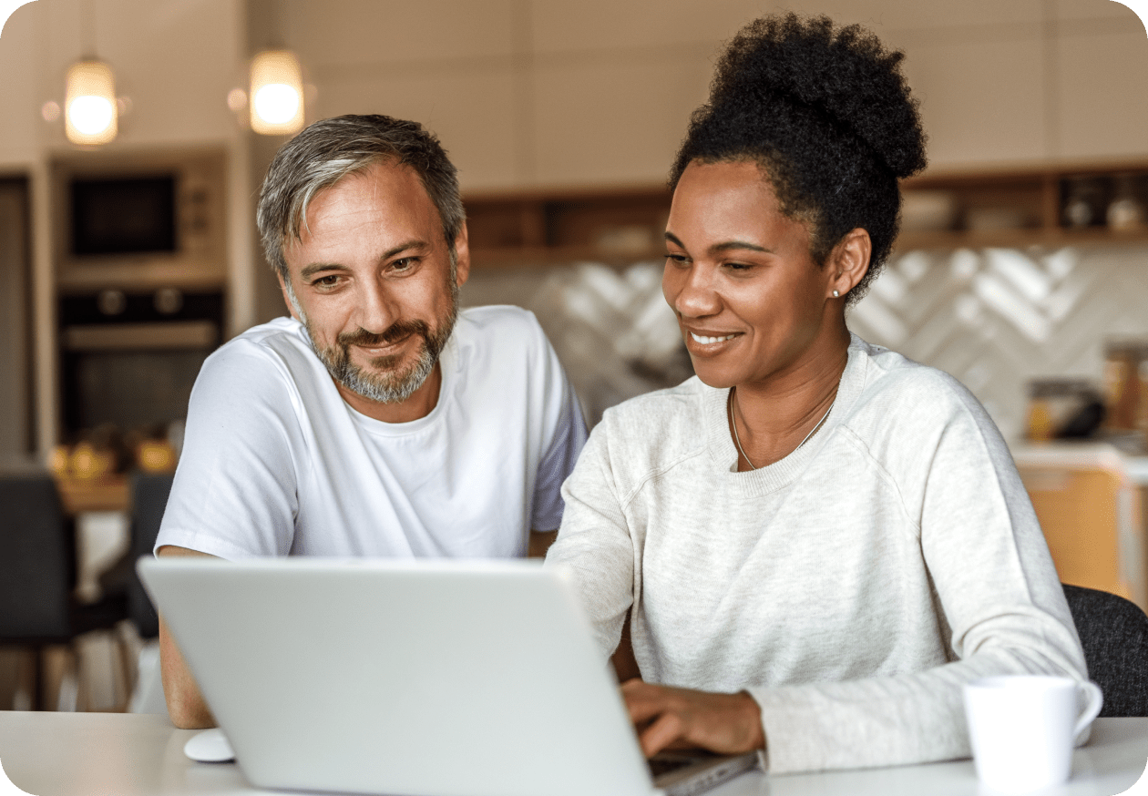 A black and white photo of a person and person sitting at a laptop.