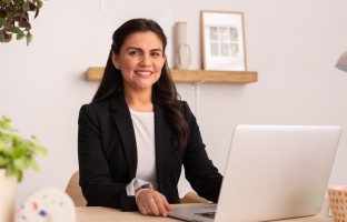 woman sitting at a desk wit her laptop looking straight at camera 