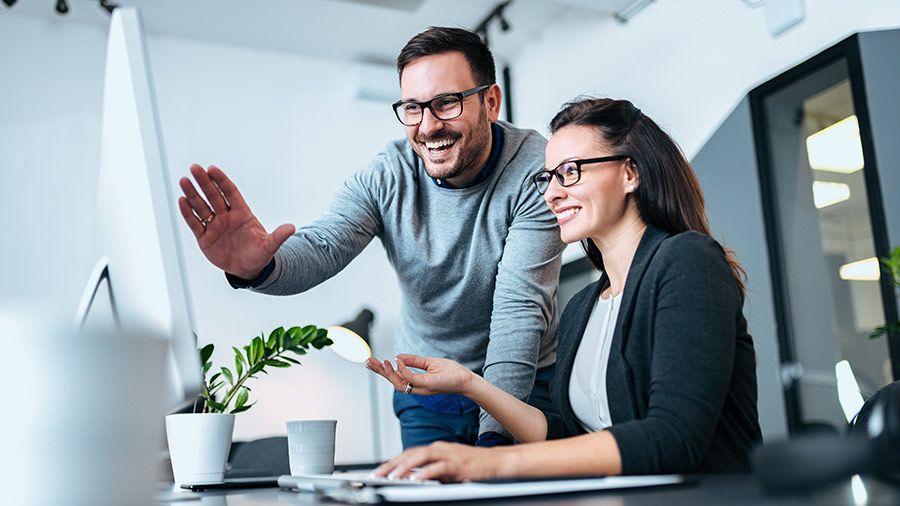 A person and person are smiling while one of them is on a laptop.