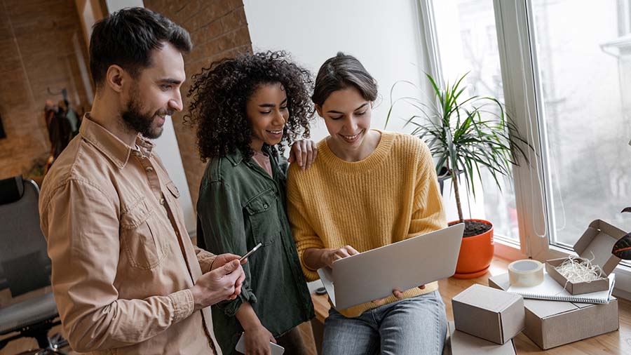 Three people are sitting around a laptop computer.