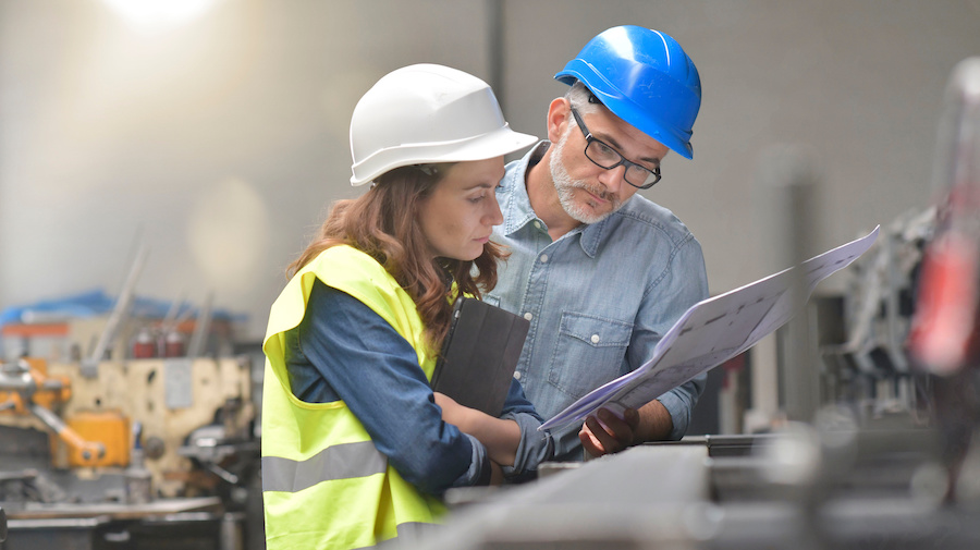 Two workers standing next to each other in front of a machine.