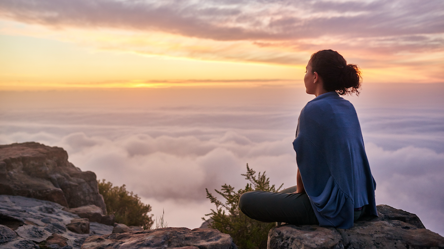 Woman staring into the clouds, on top of a mountain.