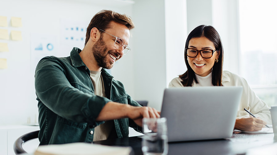 Two people sitting at a table with a laptop, reading about what's new in QuickBooks Online.