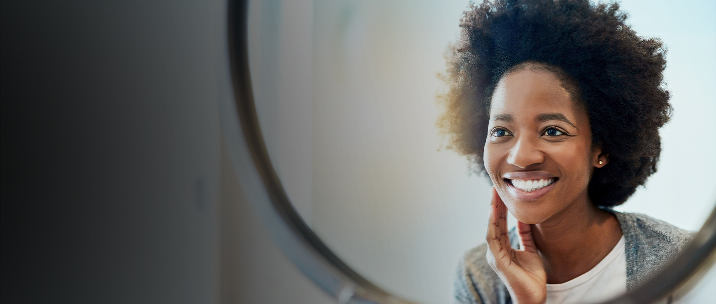 A person smiling and holding a glass with a reflection of her face in it.